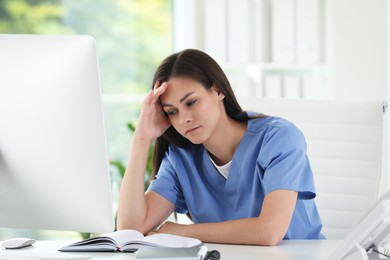 Photo of Tired nurse at table in hospital office