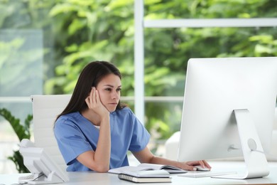 Beautiful nurse working with computer at table in hospital office