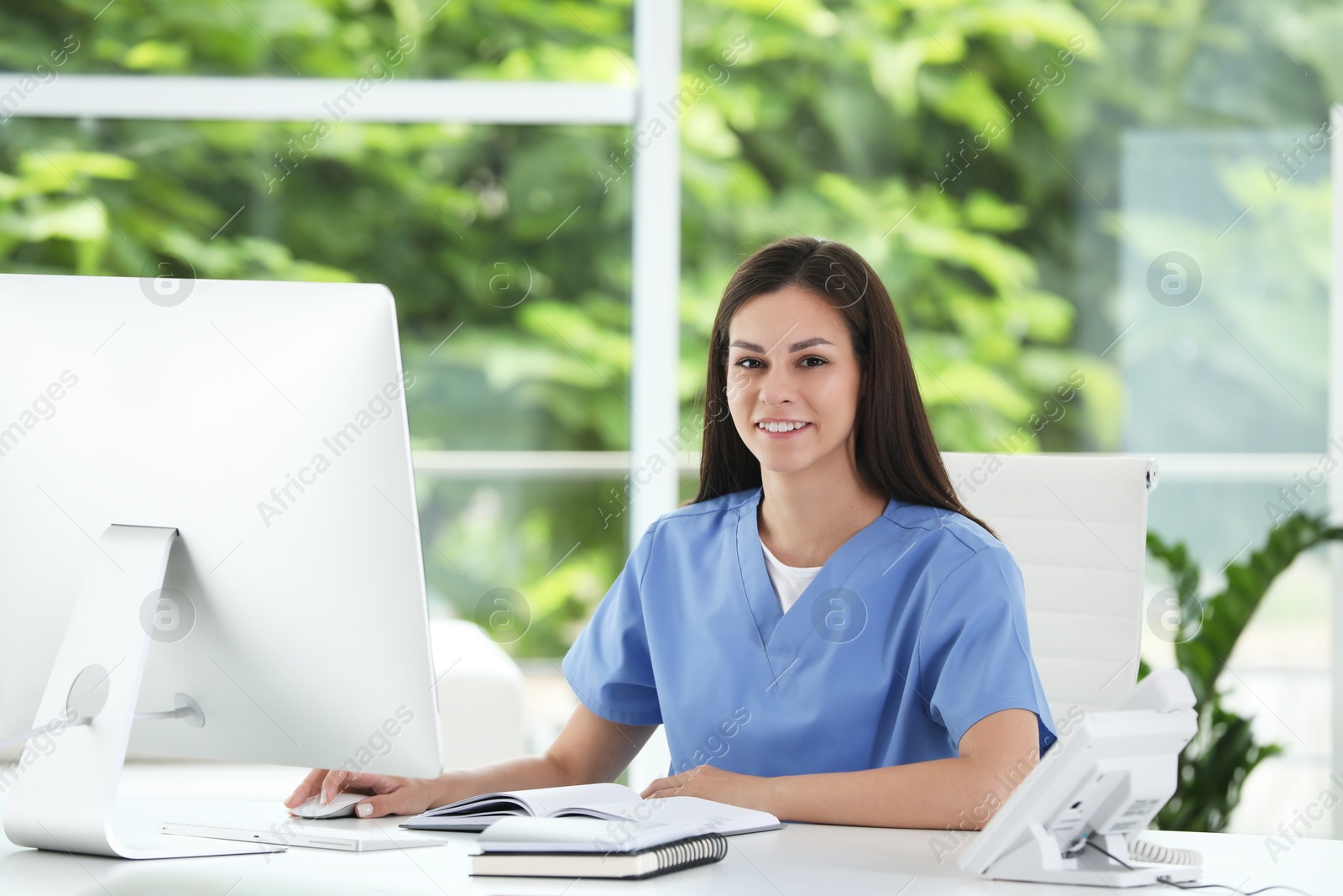 Photo of Smiling nurse working with computer at table in hospital office