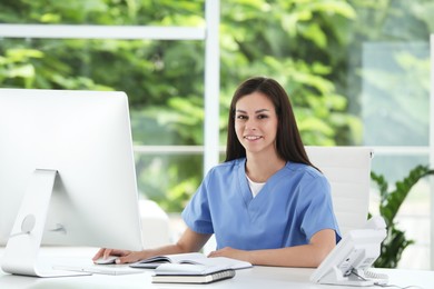 Photo of Smiling nurse working with computer at table in hospital office