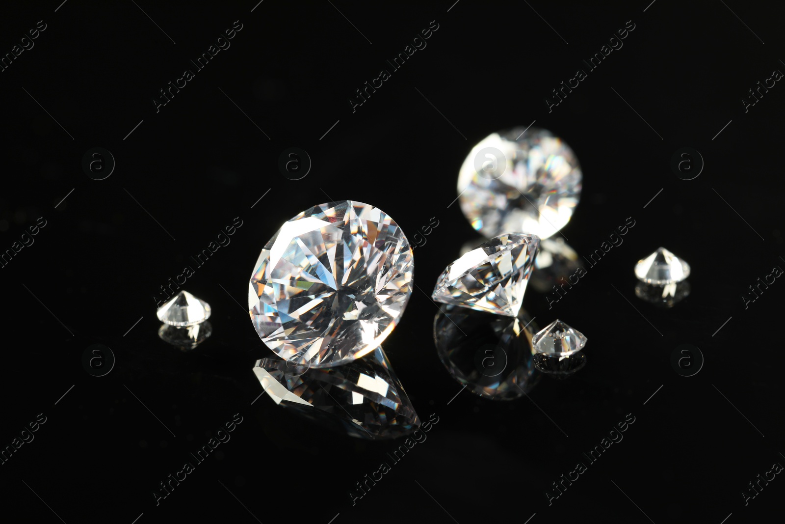 Photo of Many beautiful shiny diamonds on black mirror surface, closeup