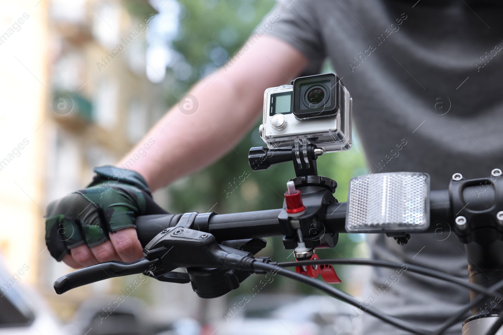 Photo of Man riding bicycle with modern action camera outdoors, closeup