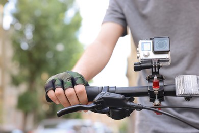 Photo of Man riding bicycle with modern action camera outdoors, closeup