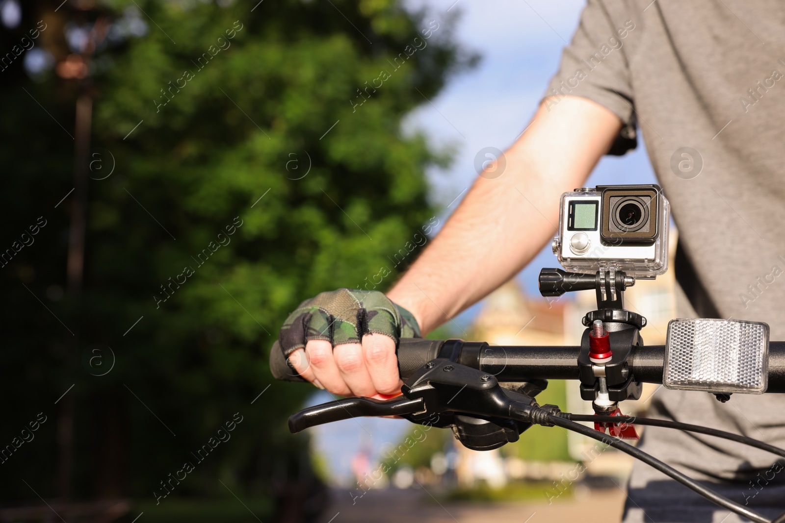 Photo of Man riding bicycle with modern action camera outdoors, closeup