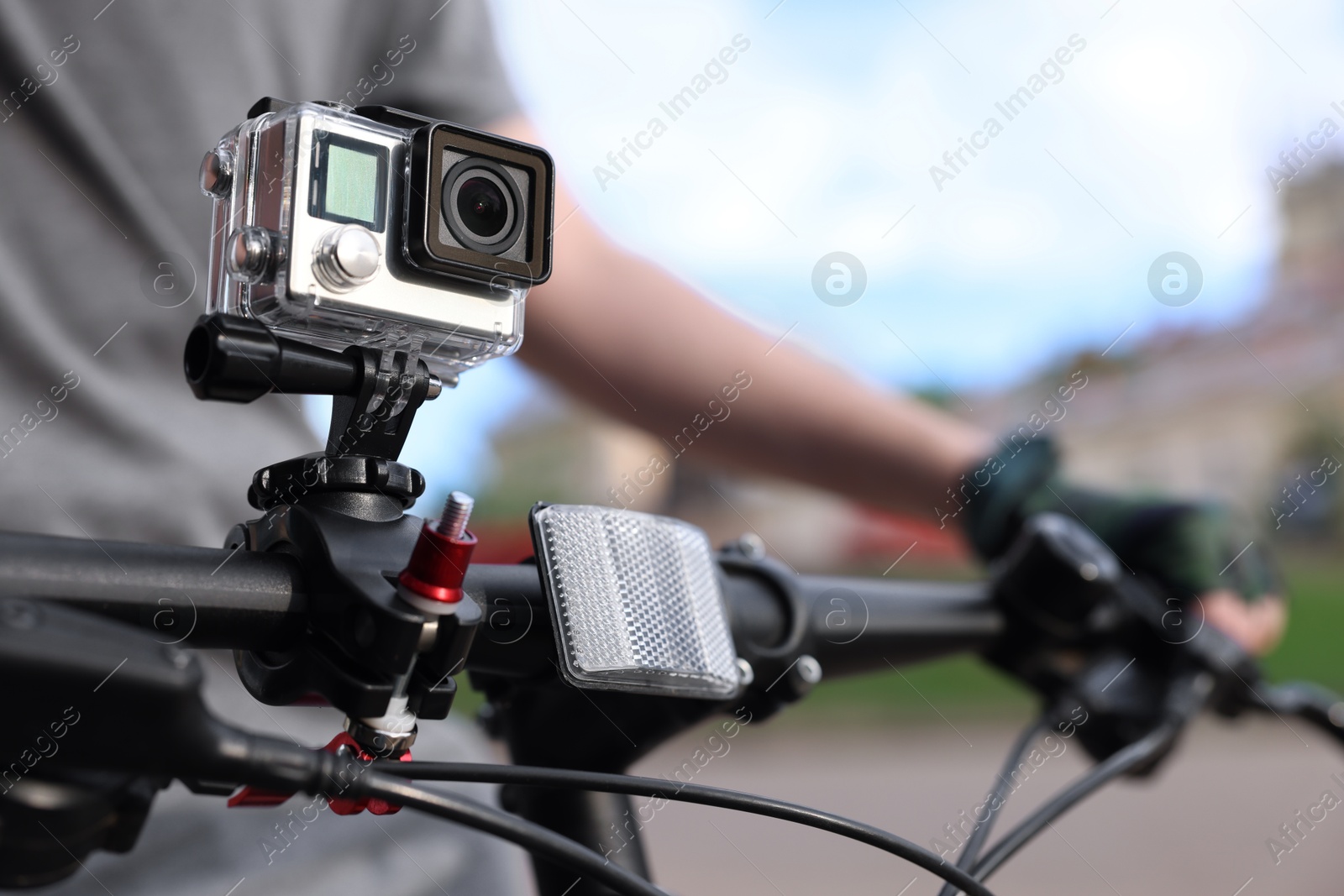 Photo of Man riding bicycle with modern action camera outdoors, closeup