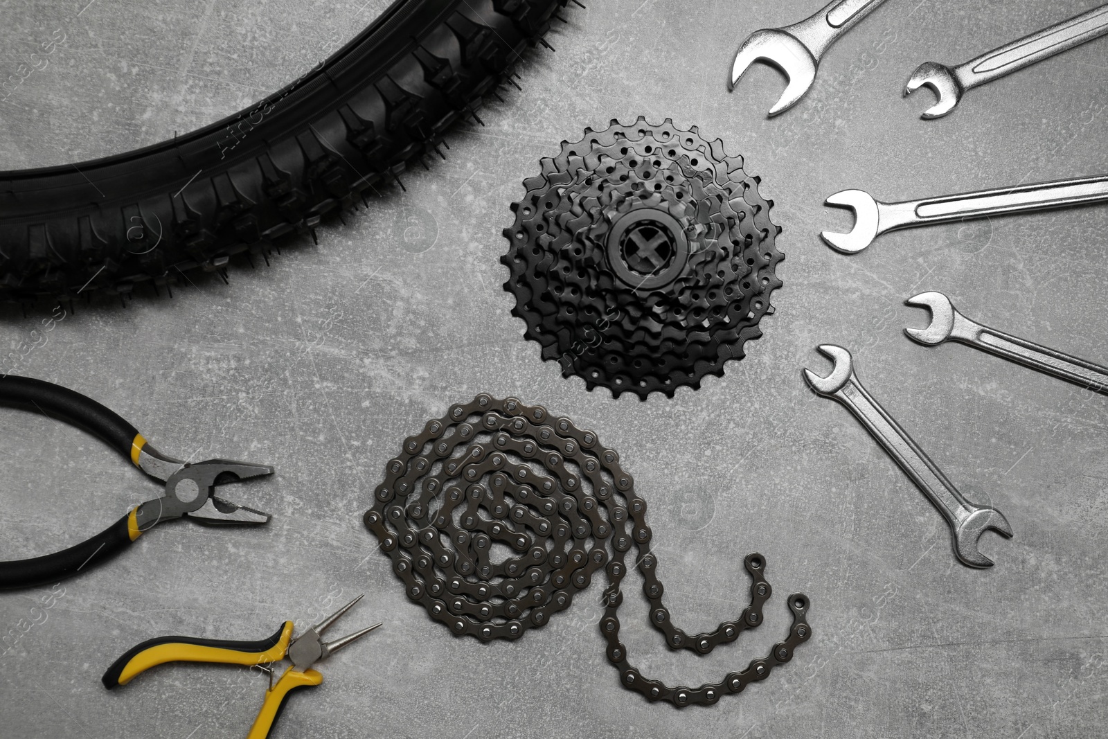 Photo of Wrenches, pliers, bicycle tire, cassette and chain on grey textured background, flat lay