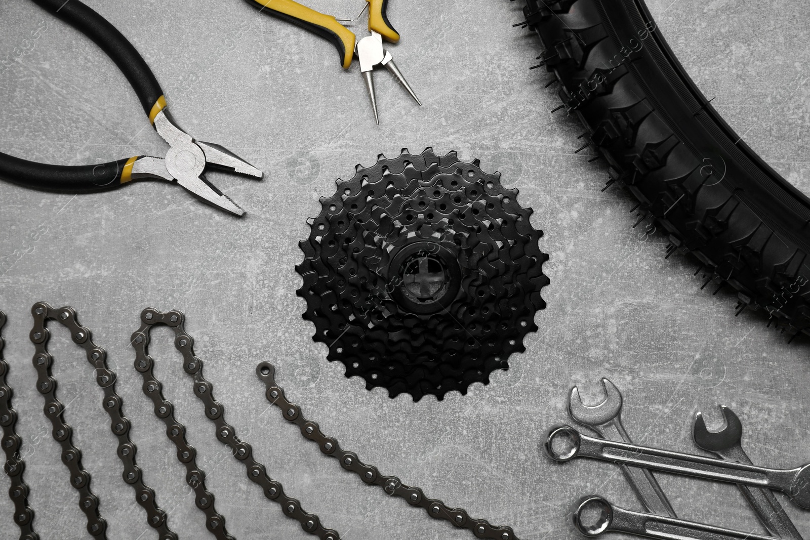 Photo of Wrenches, pliers, bicycle tire, cassette and chain on grey textured background, flat lay