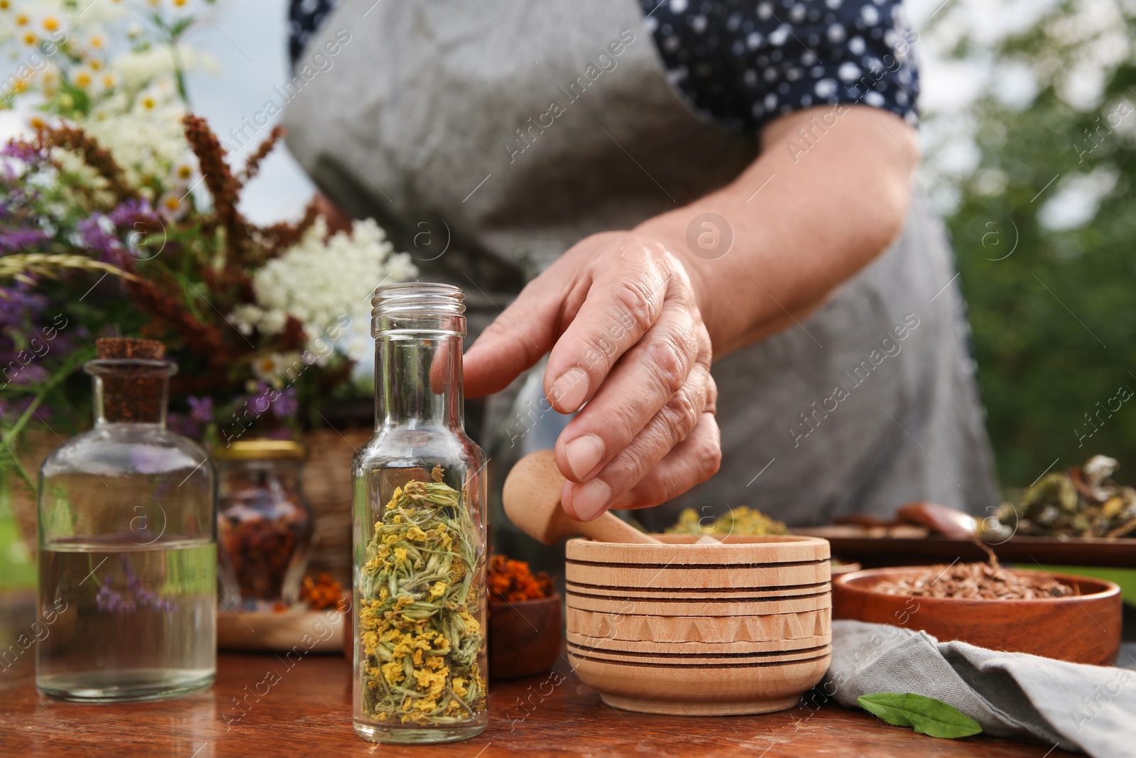 Photo of Senior woman making tincture at table outdoors, closeup