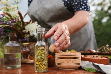 Senior woman making tincture at table outdoors, closeup