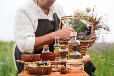 Photo of Senior woman with wildflowers outdoors, focus on different ingredients for tincture on wooden table