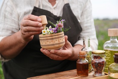 Photo of Senior woman with mortar and pestle making tincture outdoors, closeup