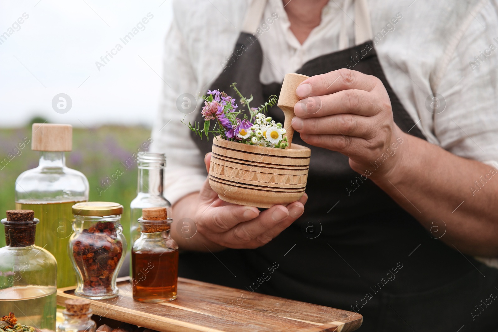 Photo of Senior woman with mortar and pestle making tincture outdoors, closeup