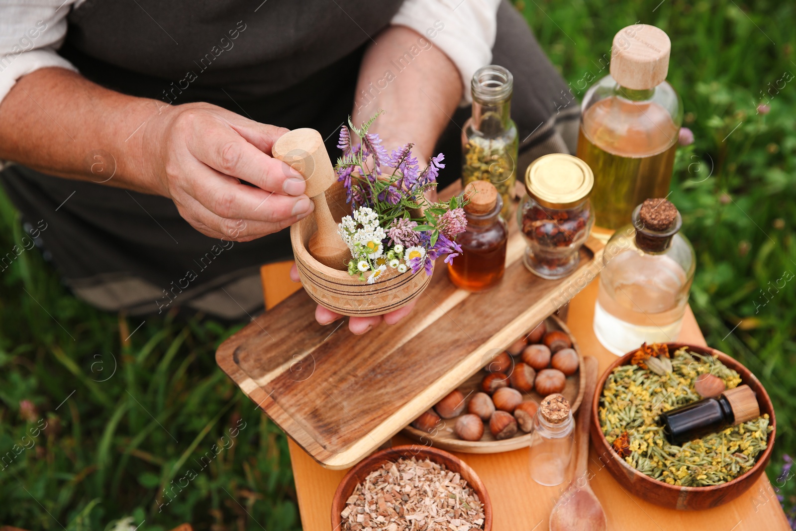 Photo of Senior woman with mortar and pestle making tincture outdoors, closeup