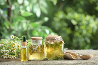 Photo of Different natural tinctures and dry daisy flowers on wooden table outdoors