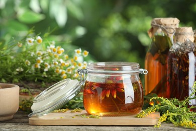 Photo of Different natural tinctures and herbs on wooden table outdoors, closeup