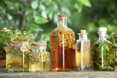 Photo of Different natural tinctures on wooden table outdoors, closeup