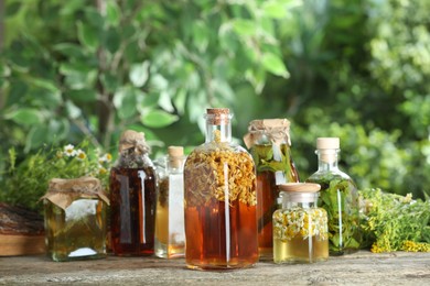 Photo of Different natural tinctures and herbs on wooden table outdoors