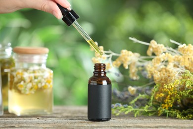 Photo of Woman dripping tincture from pipette into bottle at wooden table against blurred green background, closeup