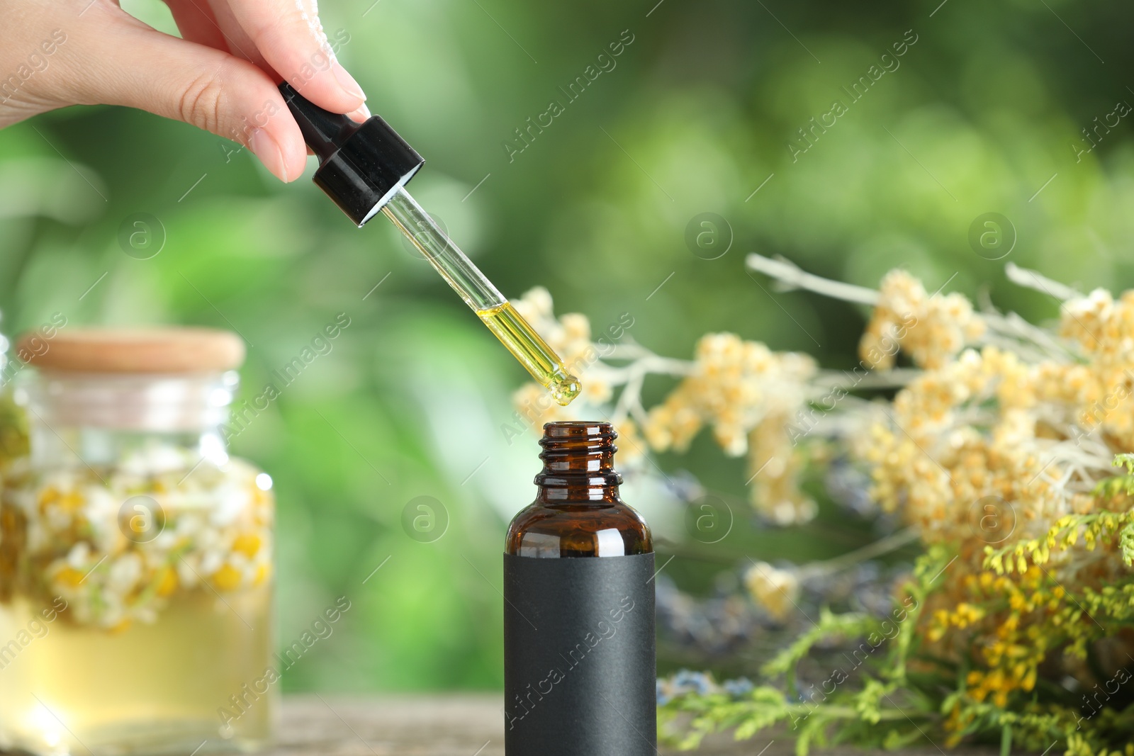 Photo of Woman dripping tincture from pipette into bottle against blurred green background, closeup