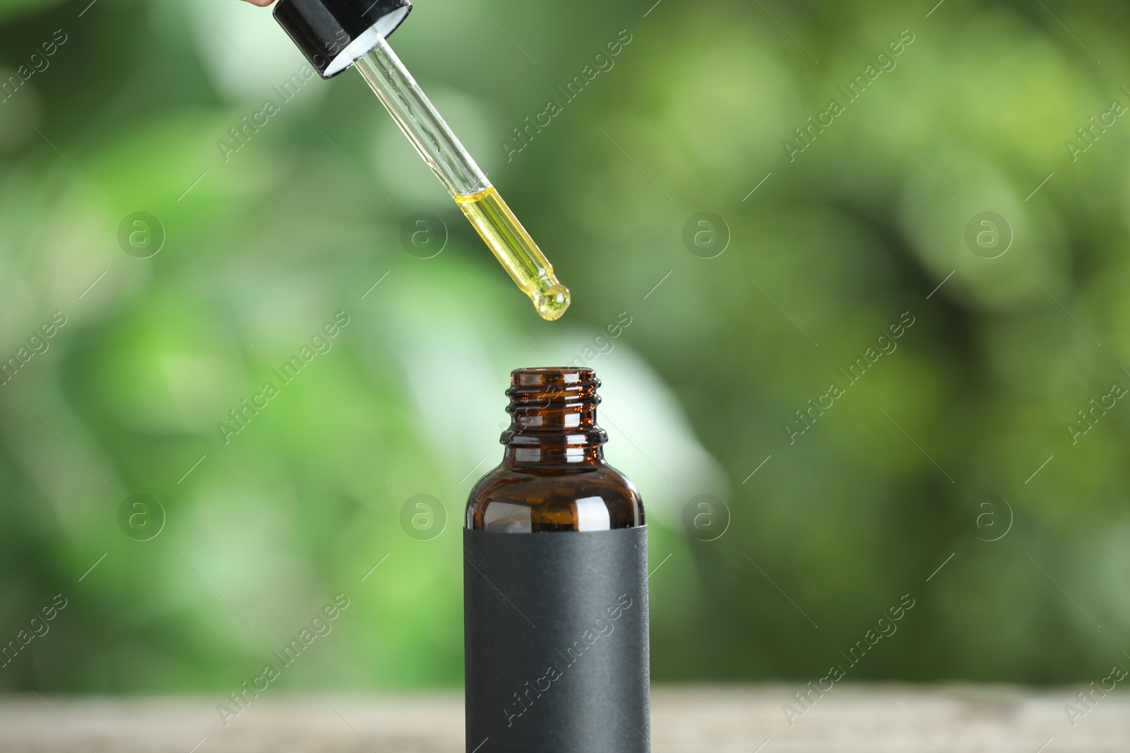 Photo of Dripping tincture from pipette into bottle against blurred green background, closeup