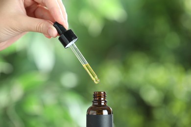 Photo of Woman dripping tincture from pipette into bottle against blurred green background, closeup