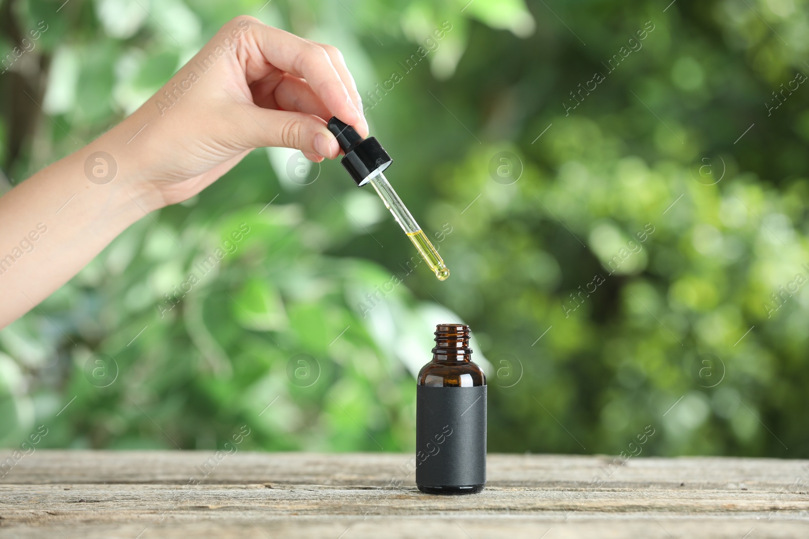 Photo of Woman dripping tincture from pipette into bottle at wooden table against blurred green background, closeup