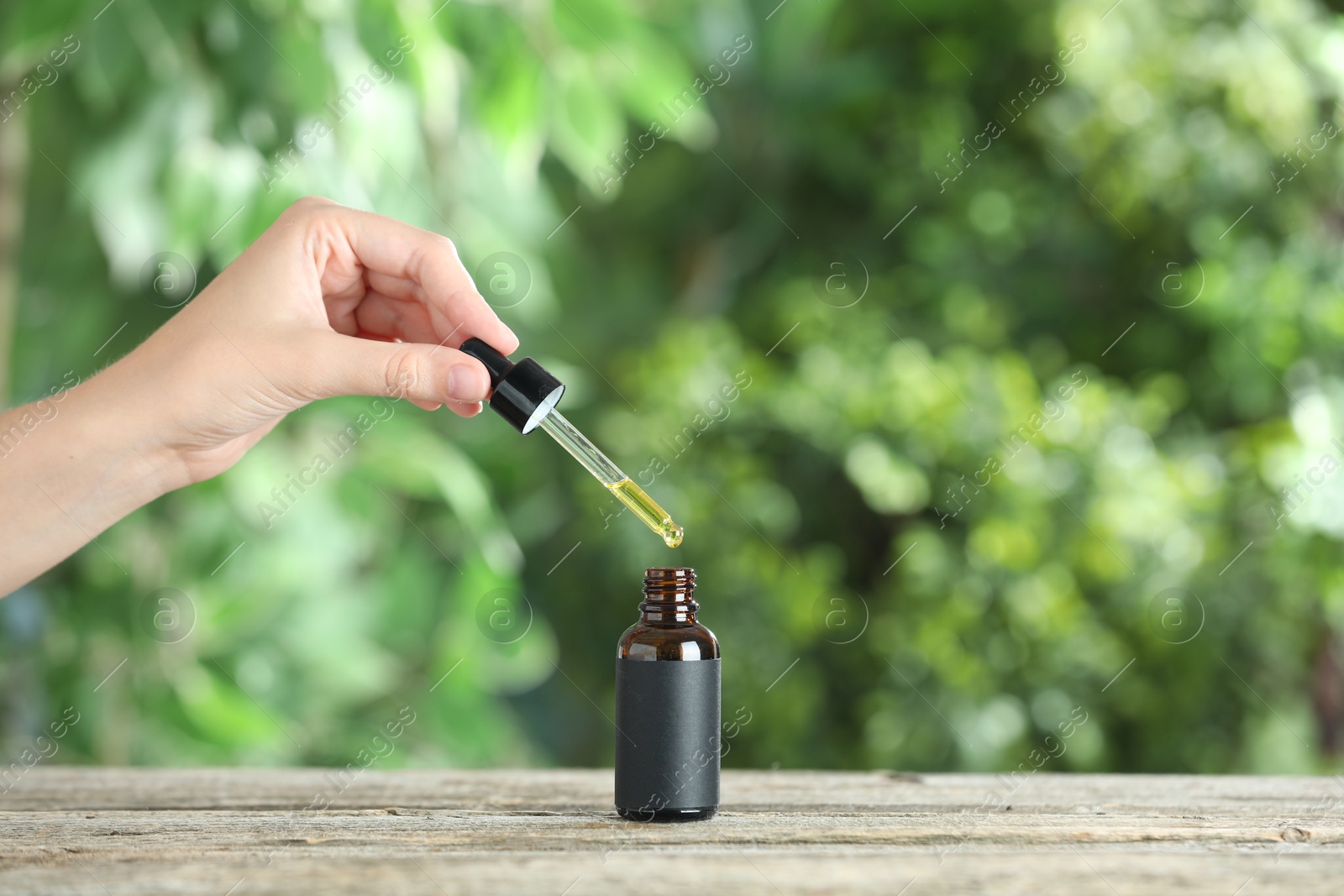 Photo of Woman dripping tincture from pipette into bottle at wooden table against blurred green background, closeup