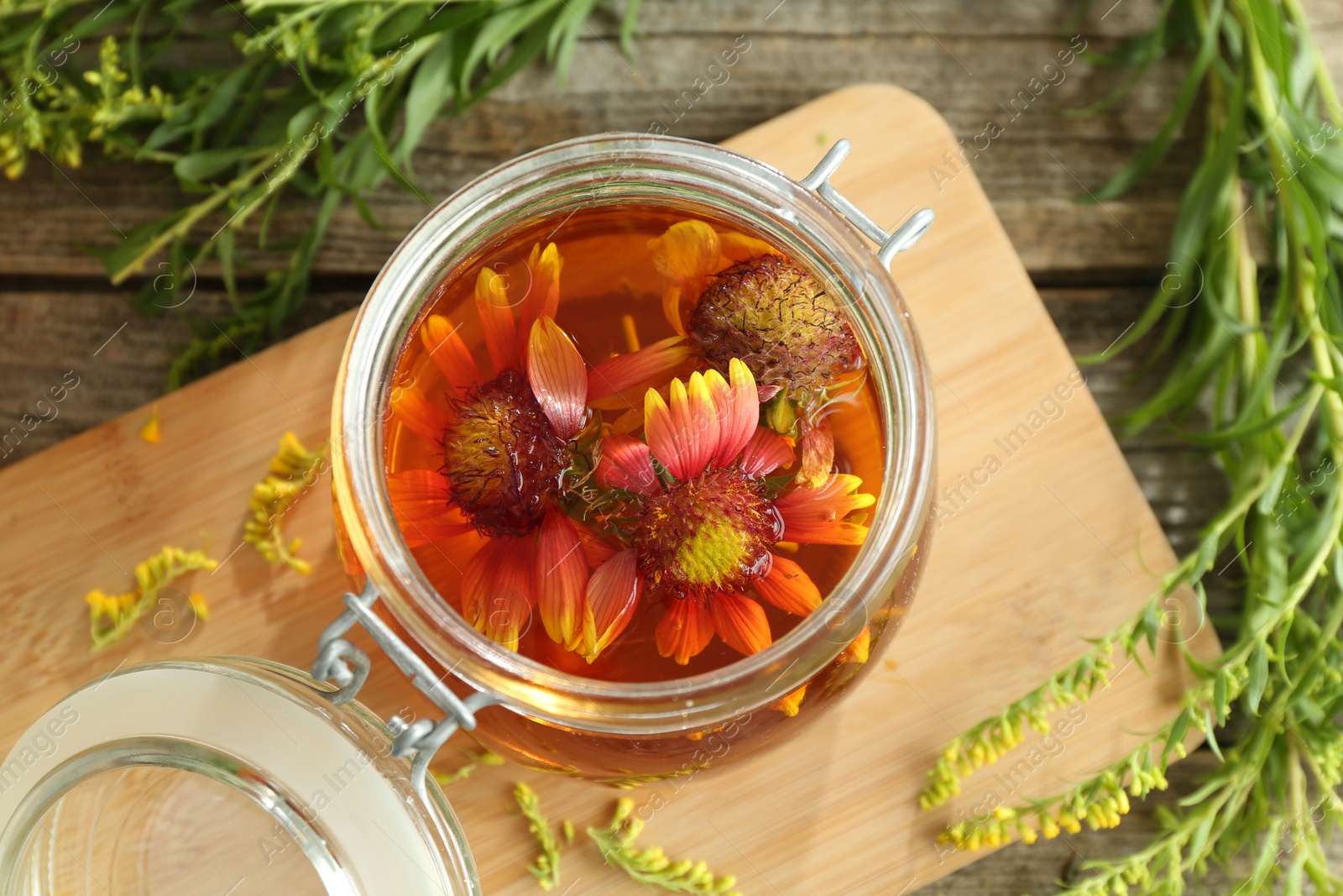 Photo of Natural tincture in jar with flowers and herbs on wooden table, above view