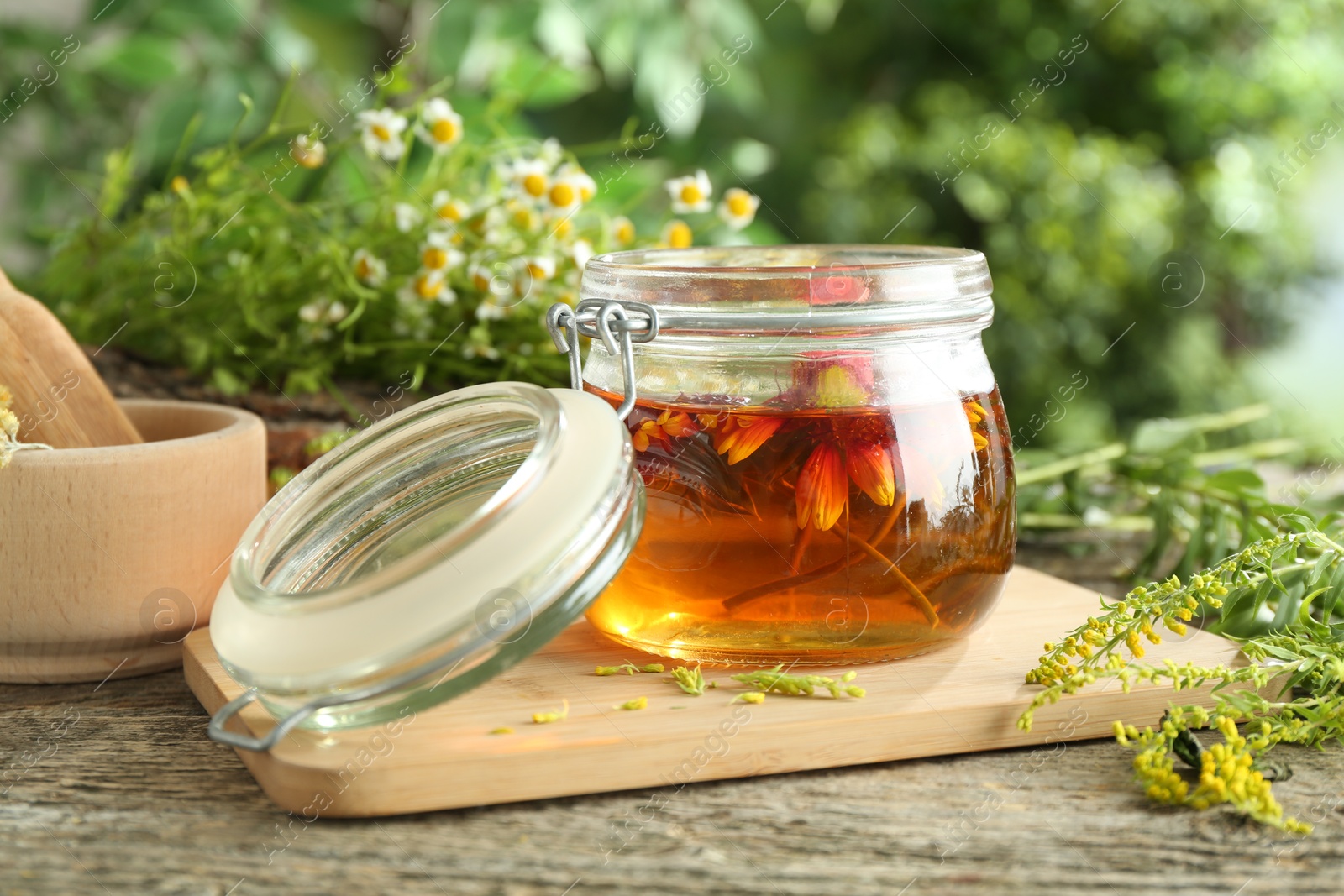 Photo of Natural tincture in jar with flowers and herbs on wooden table