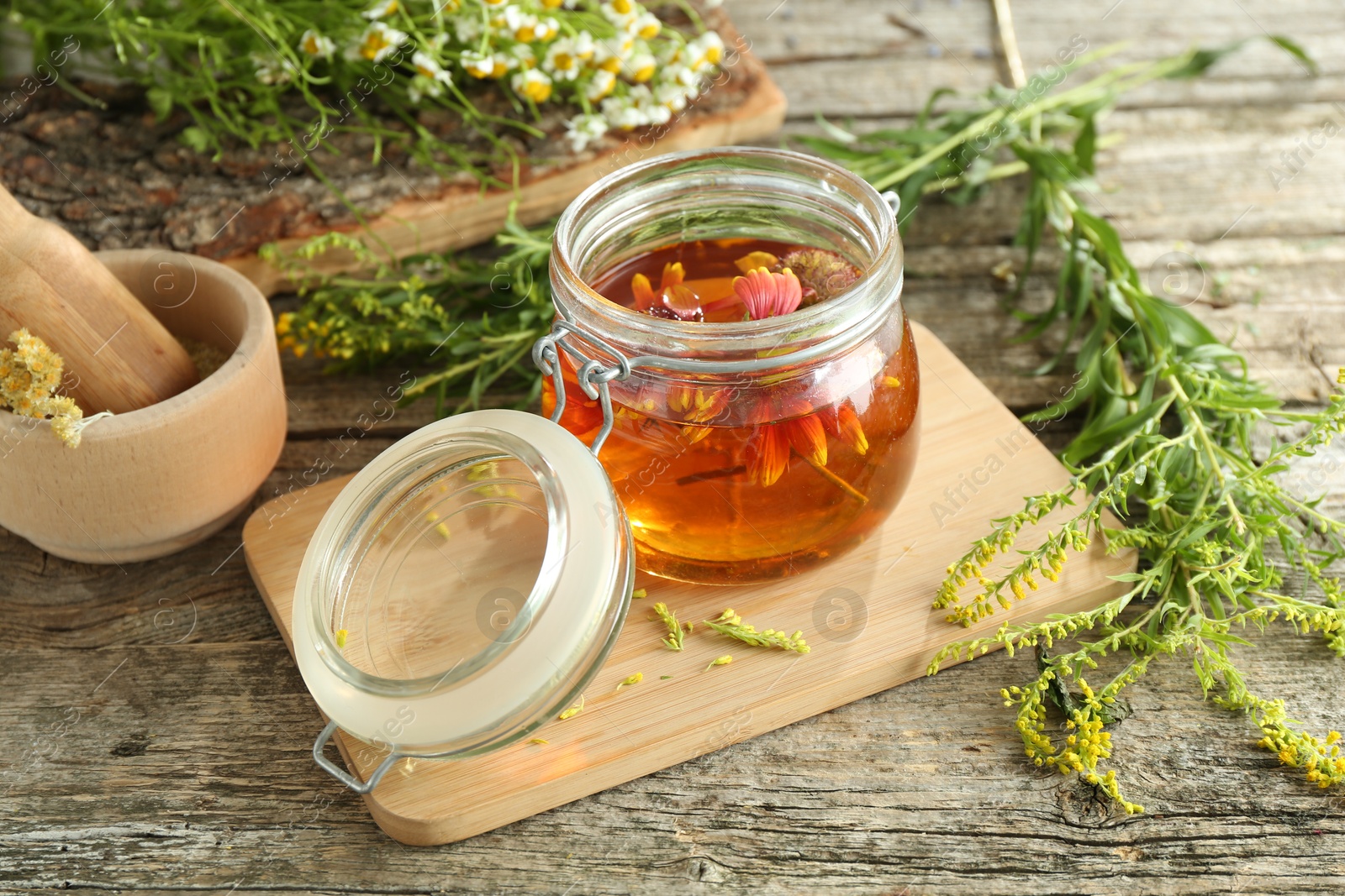 Photo of Natural tincture in jar with flowers and herbs on wooden table