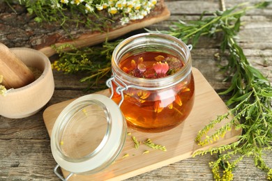 Photo of Natural tincture in jar with flowers and herbs on wooden table