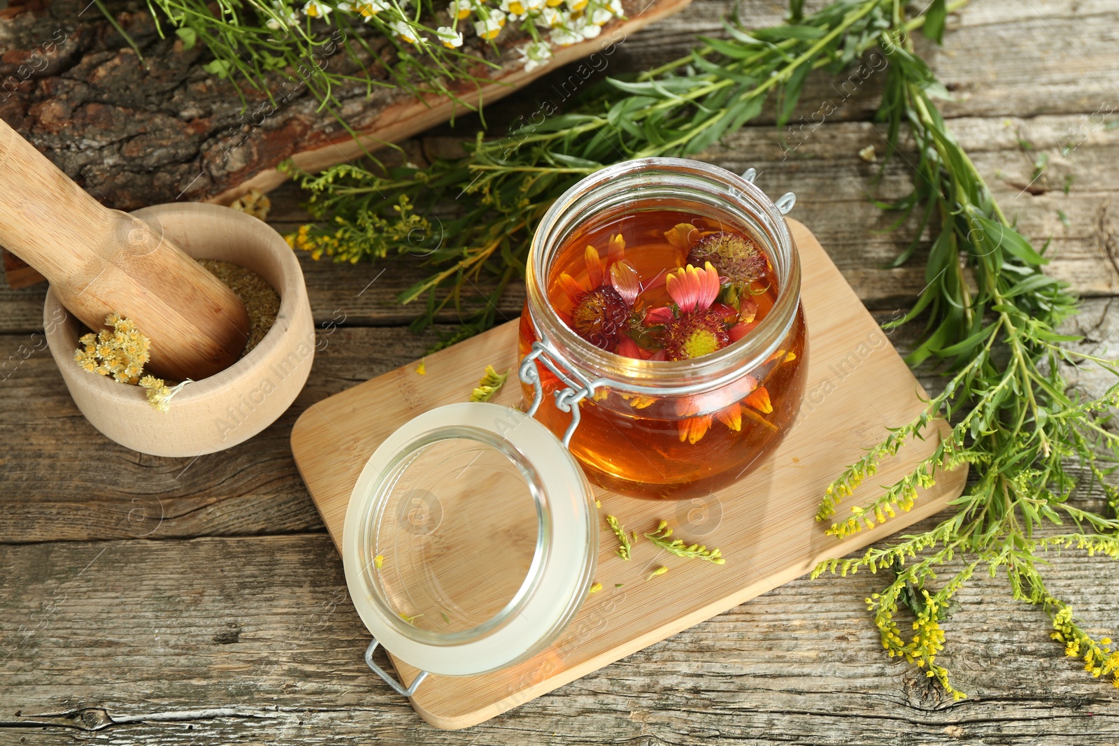 Photo of Natural tincture in jar with flowers and herbs on wooden table