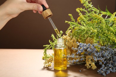 Woman dripping tincture from pipette into bottle and herbs on color background, closeup