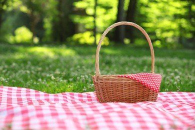 Photo of One picnic wicker basket with checkered napkin and blanket on green grass. Space for text