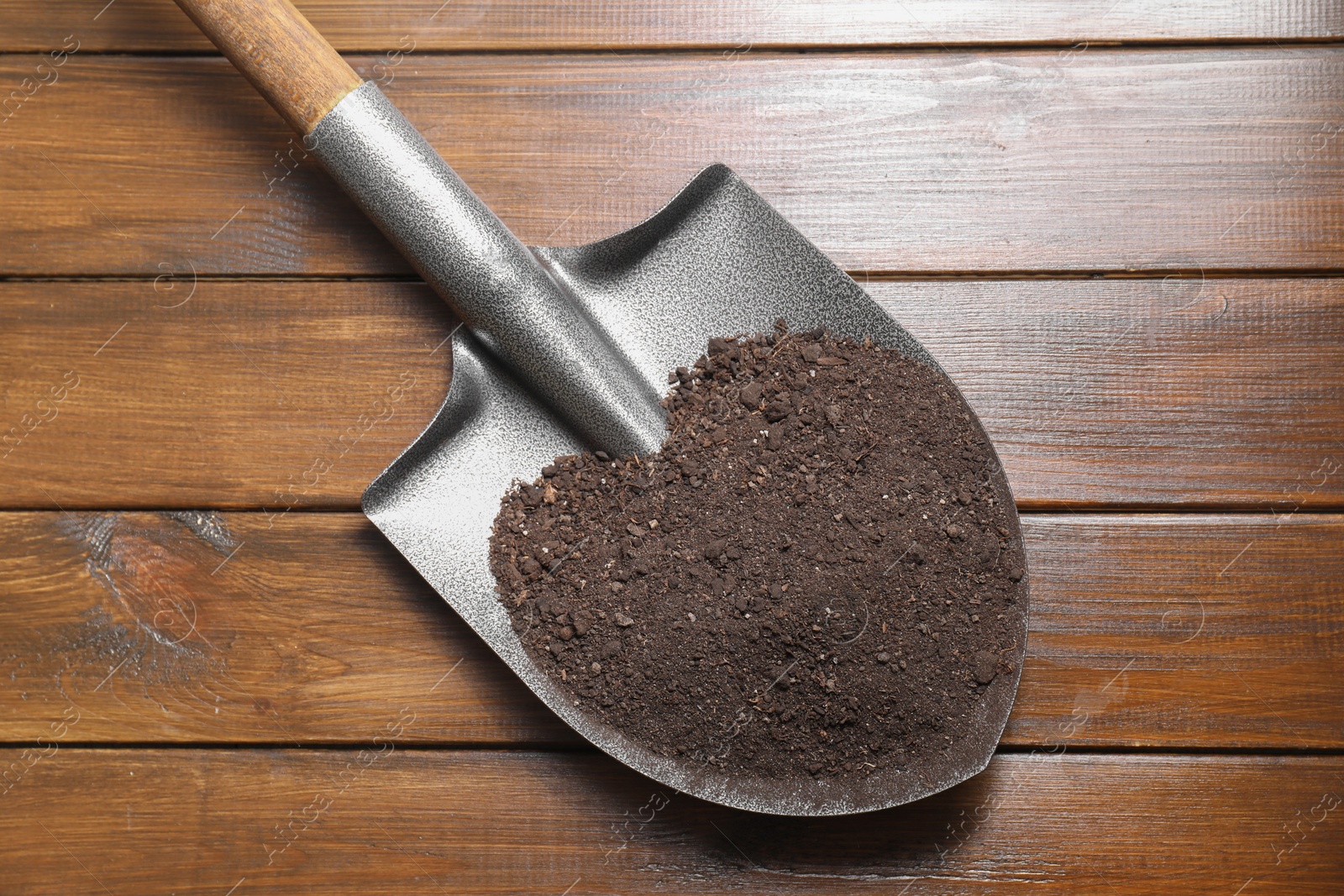 Photo of Metal shovel with soil on wooden table, top view