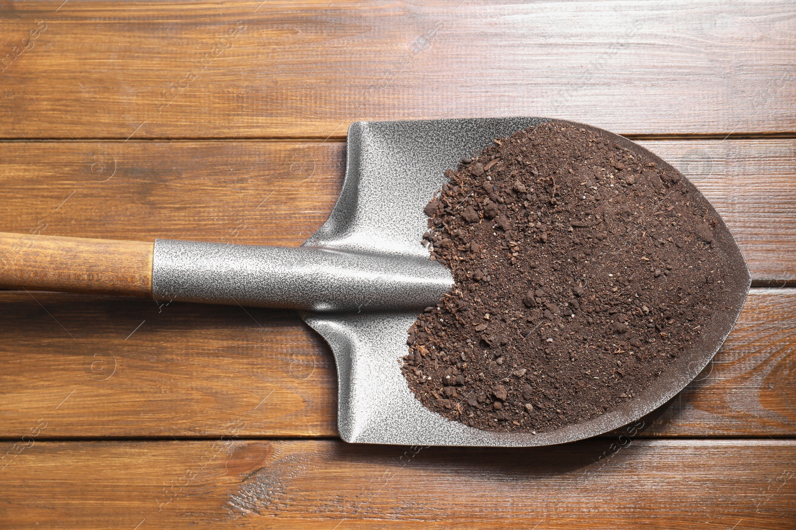 Photo of Metal shovel with soil on wooden table, top view