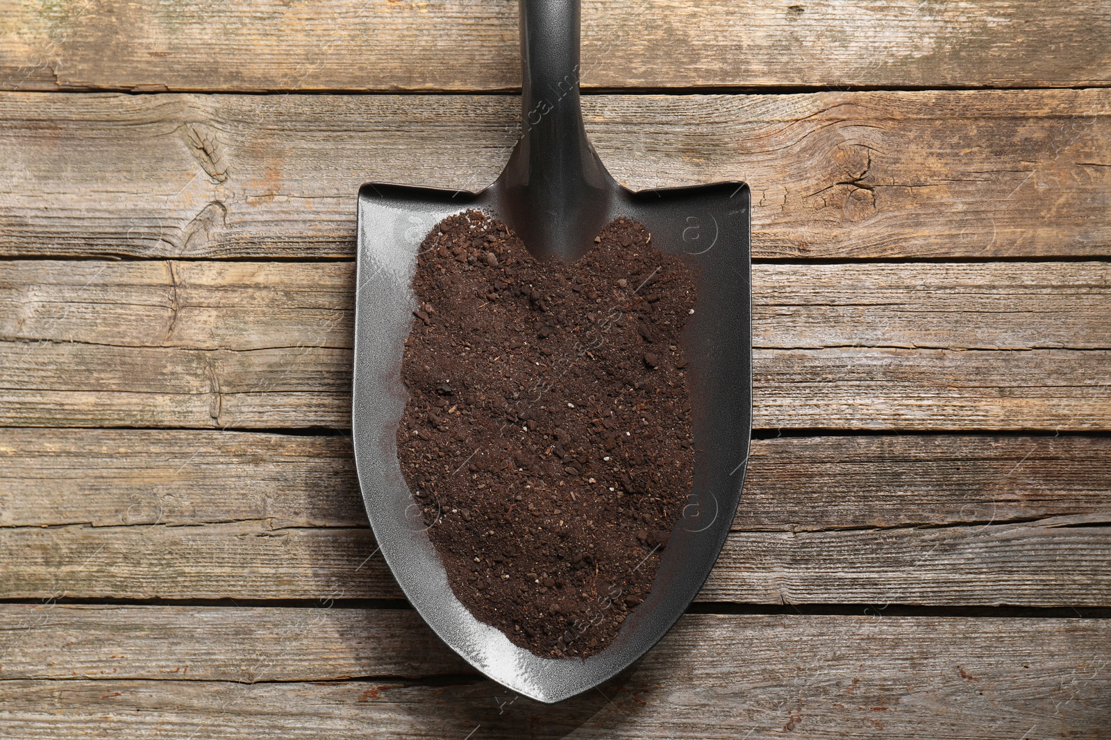 Photo of Metal shovel with soil on wooden table, top view