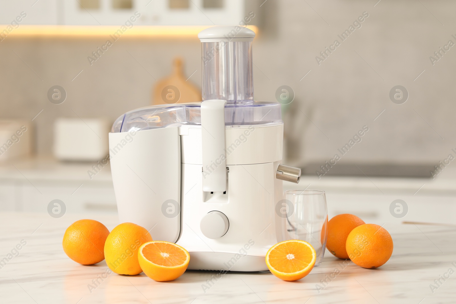 Photo of Modern juicer, oranges and glass on white marble table in kitchen