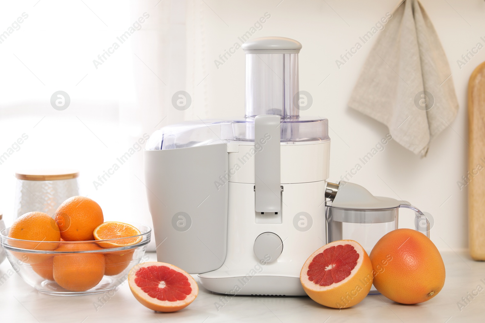 Photo of Modern juicer and grapefruits on white counter in kitchen