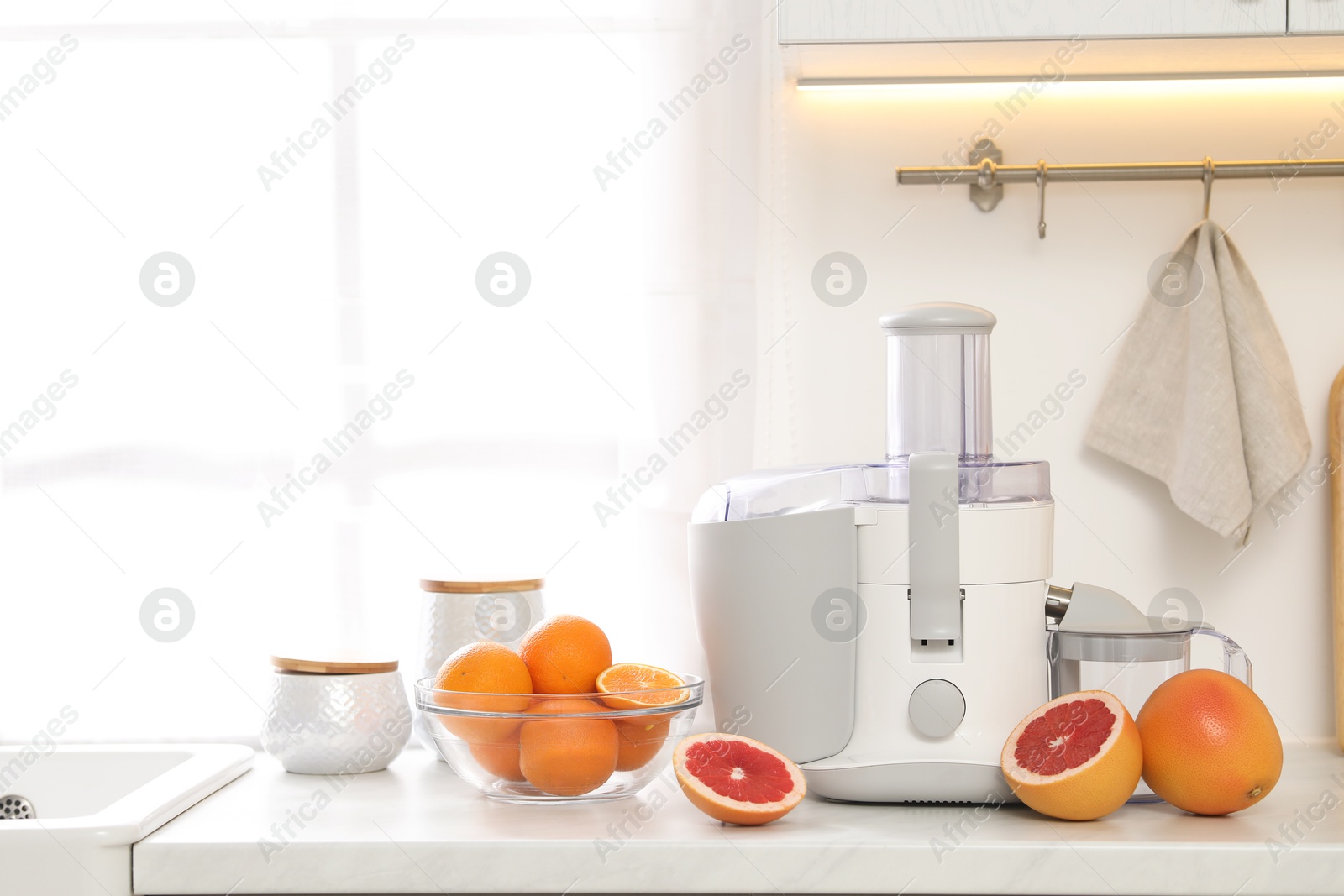 Photo of Modern juicer and grapefruits on white counter in kitchen