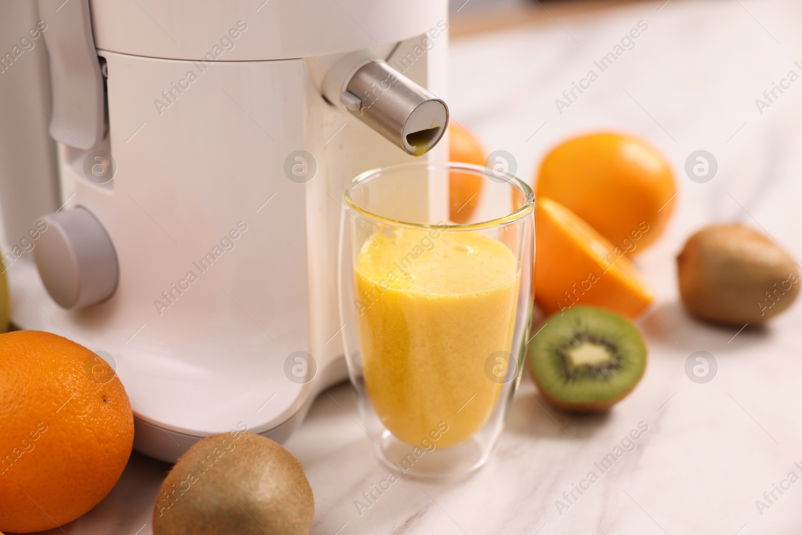 Photo of Modern juicer, fresh fruits and glass on white marble table in kitchen, closeup