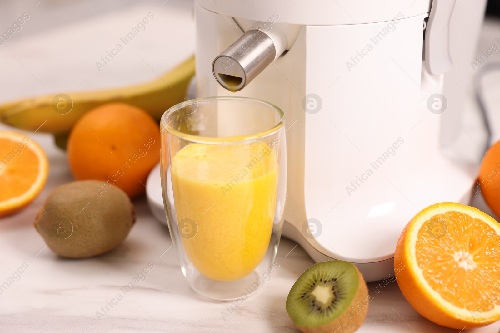 Photo of Modern juicer, fresh fruits and glass on white marble table in kitchen, closeup