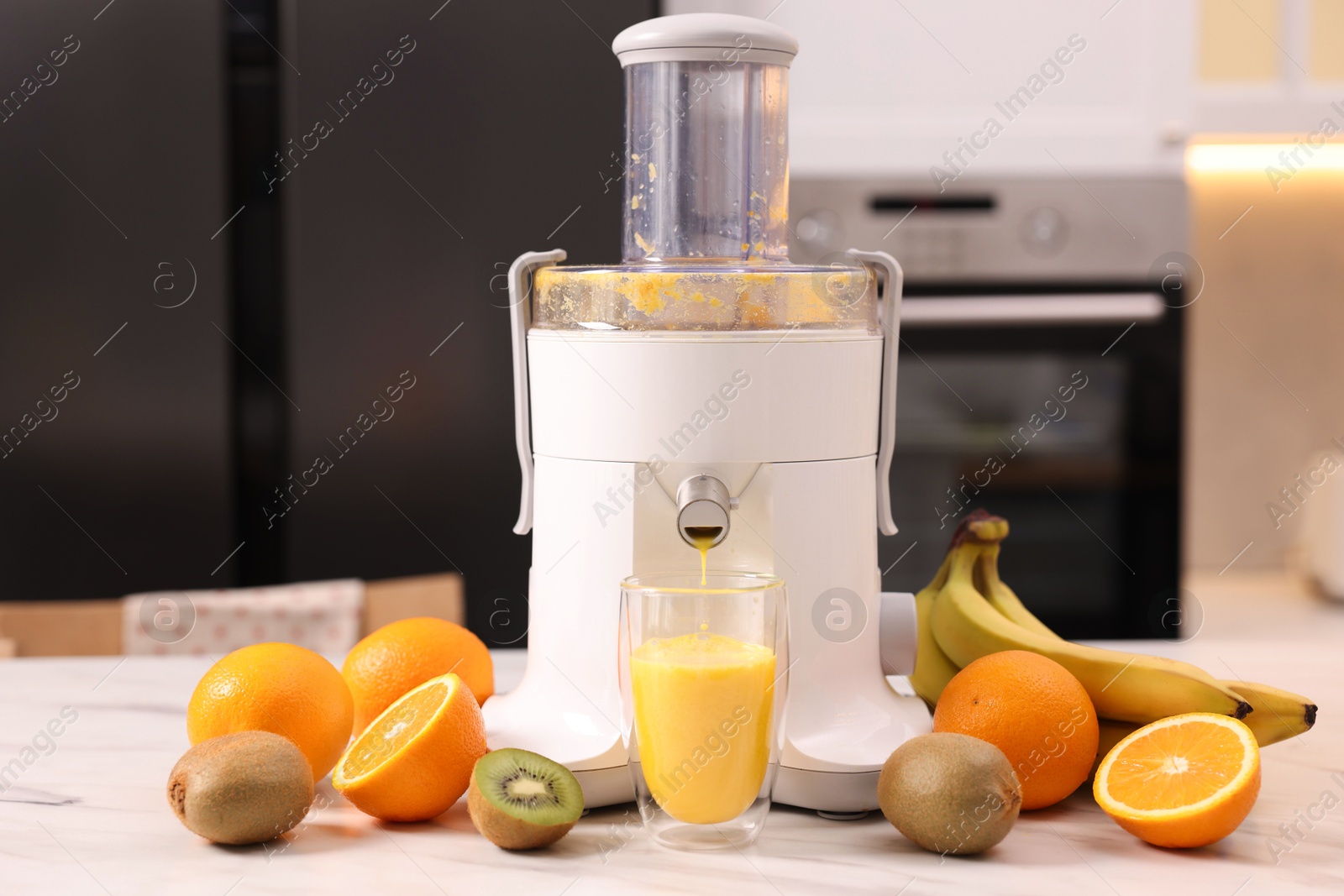 Photo of Modern juicer, fresh fruits and glass on white marble table in kitchen