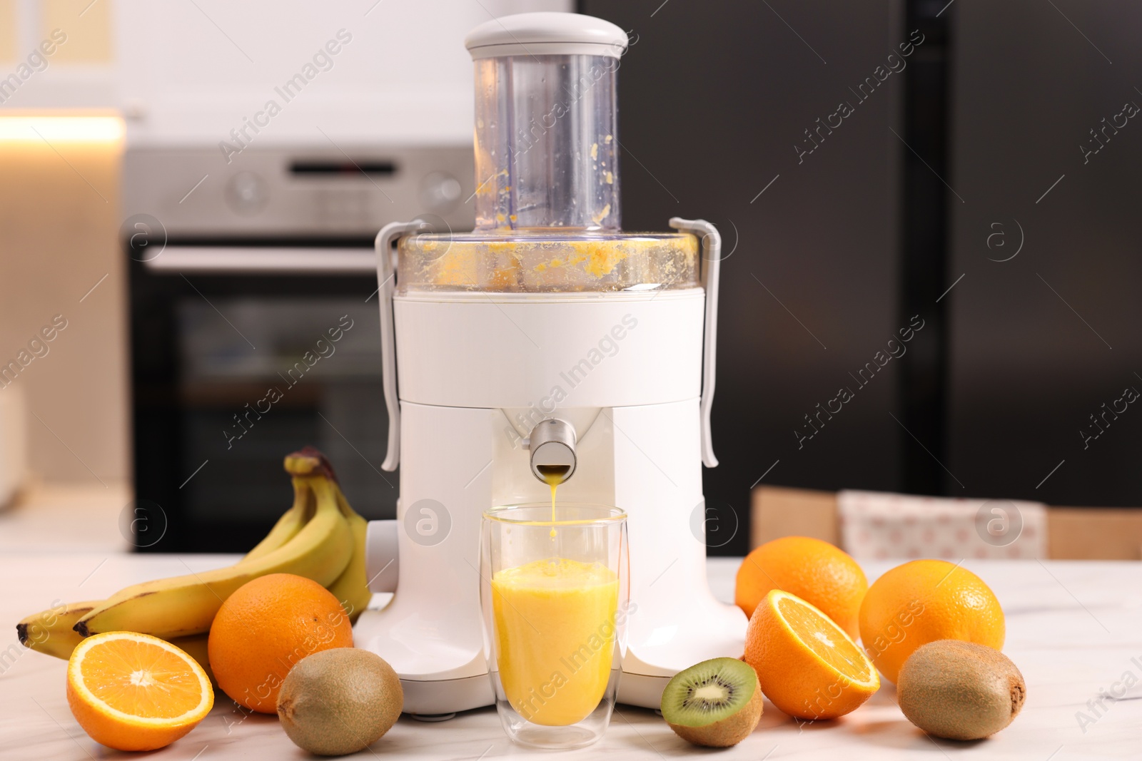 Photo of Modern juicer, fresh fruits and glass on white marble table in kitchen