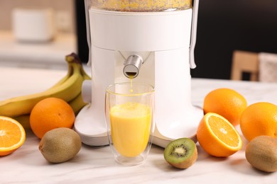 Photo of Modern juicer, fresh fruits and glass on white marble table in kitchen, closeup