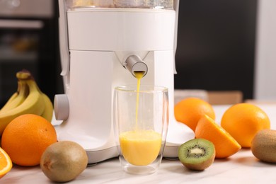 Modern juicer, fresh fruits and glass on white marble table in kitchen, closeup