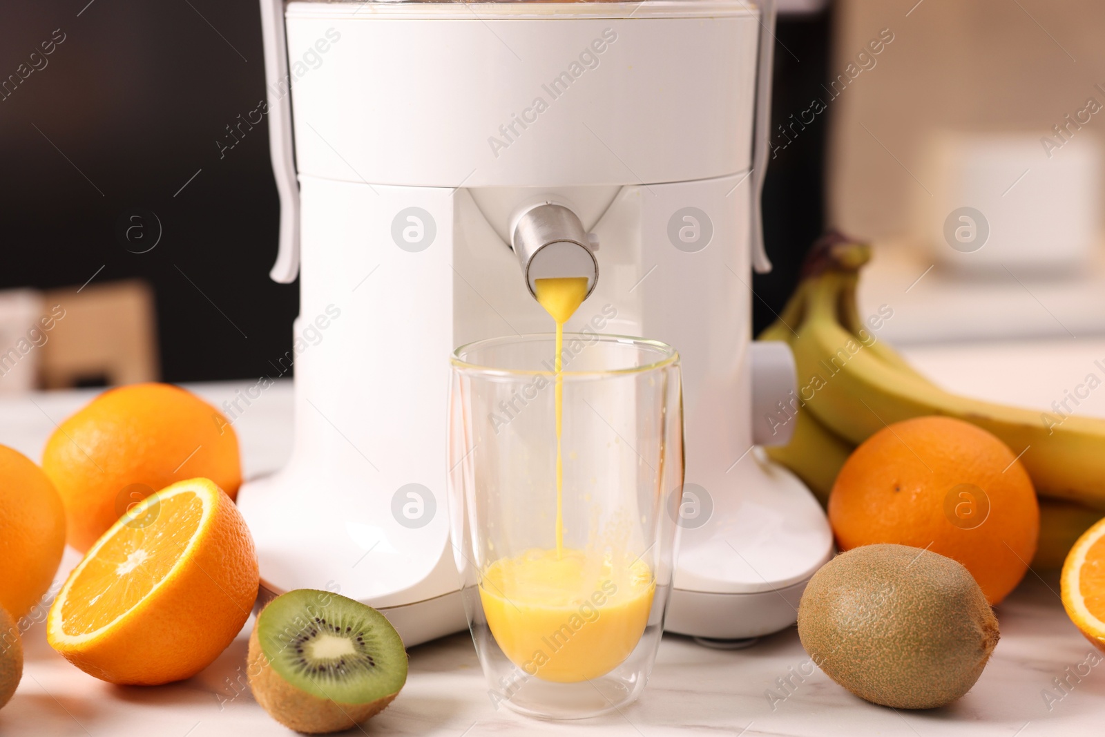 Photo of Modern juicer, fresh fruits and glass on white marble table in kitchen, closeup