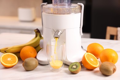 Photo of Modern juicer, fresh fruits and glass on white marble table in kitchen, closeup