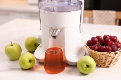 Photo of Modern juicer, fresh fruits and glass on white marble table in kitchen