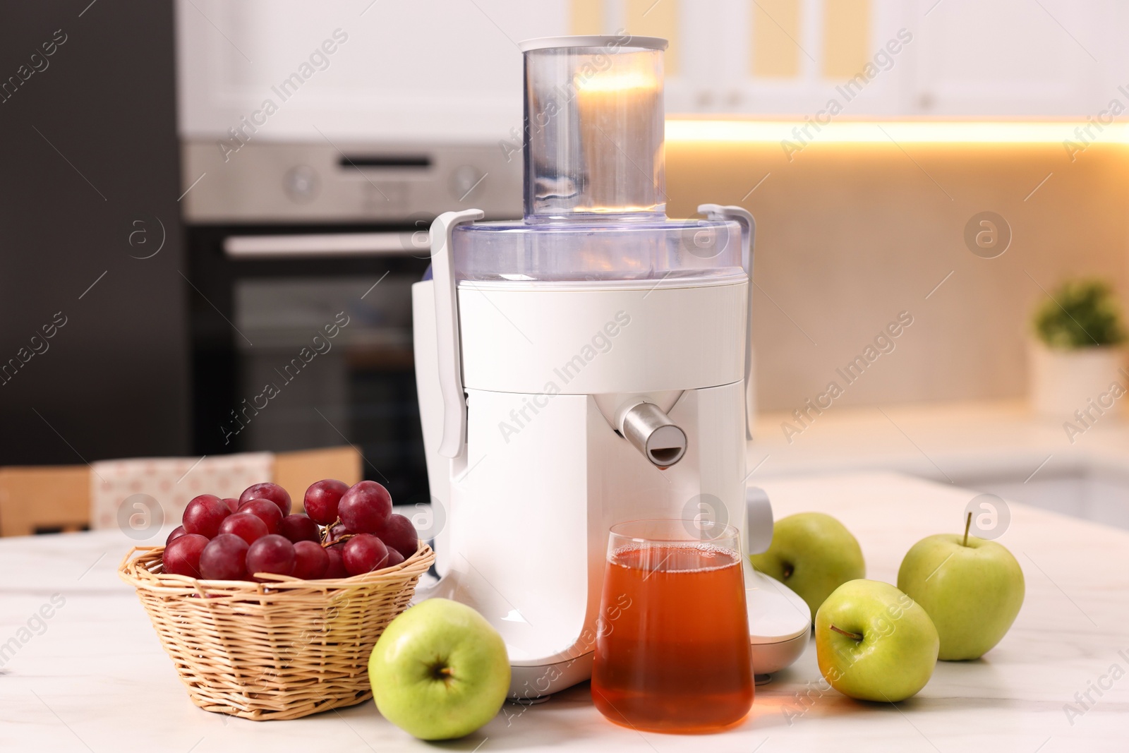 Photo of Modern juicer, fresh fruits and glass on white marble table in kitchen